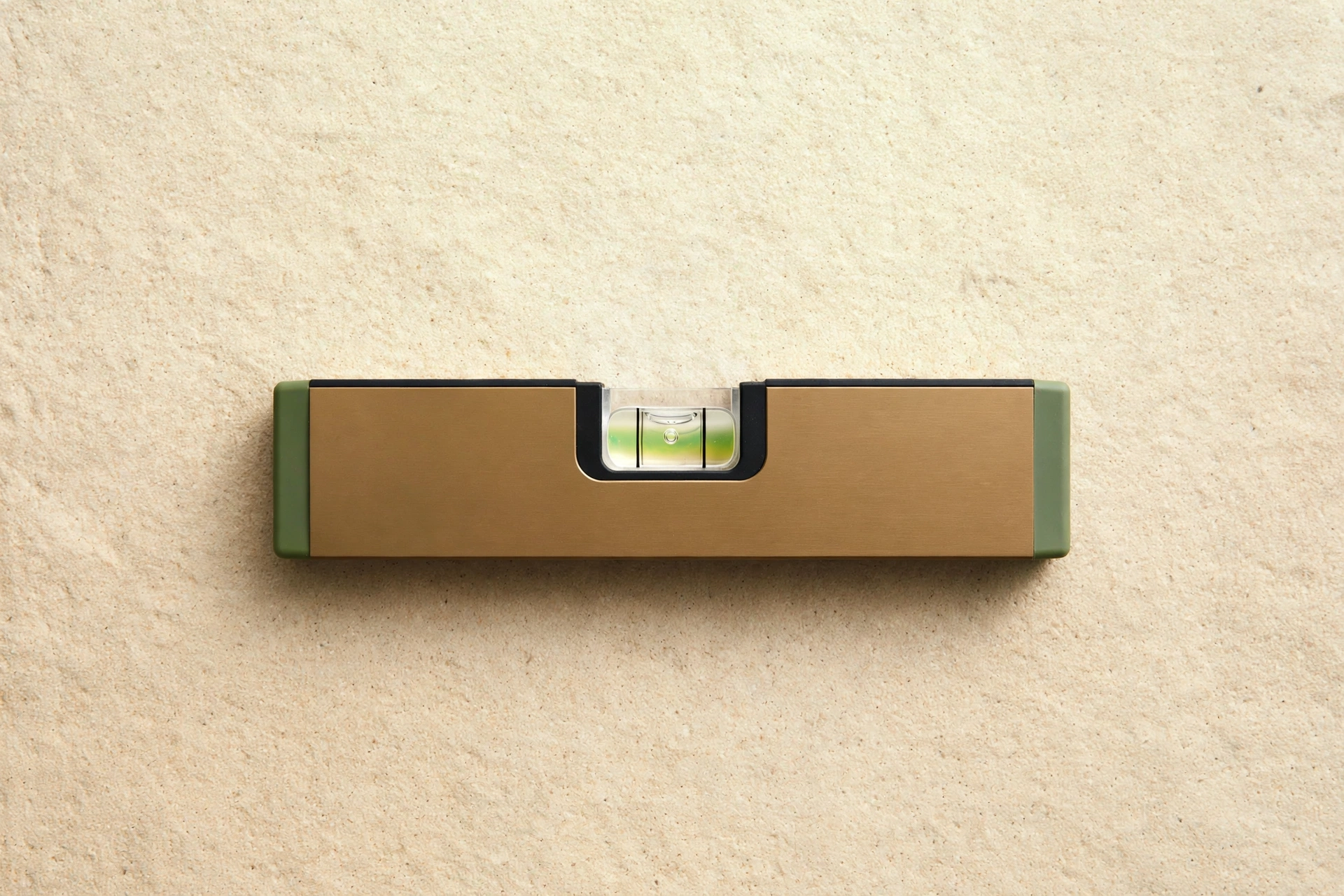 Nivel de burbuja bronce y verde salvia sobre superficie de piedra clara, símbolo de calibración